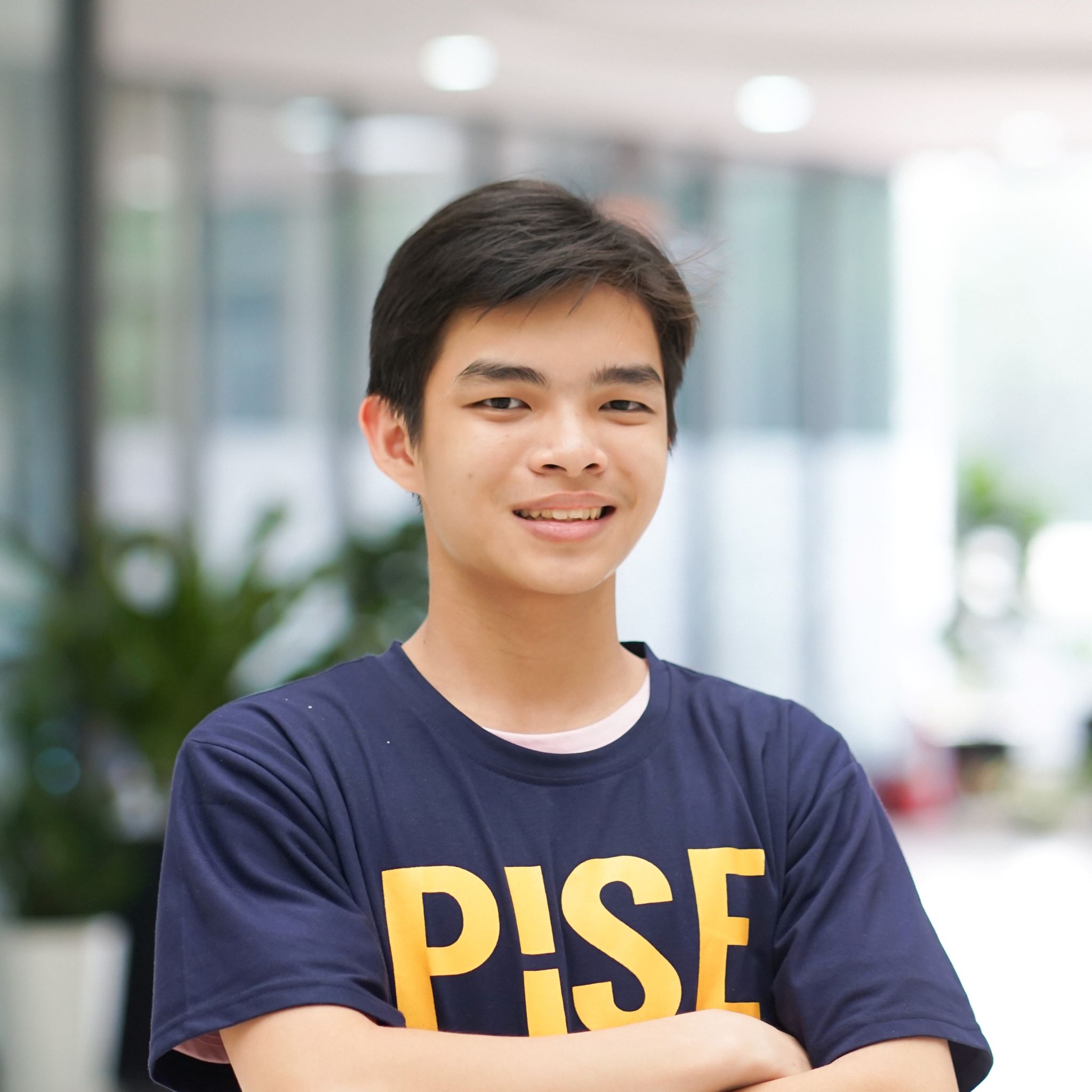 Tien-Thanh Hua smiling in a dark blue T-shirt with “PISE” logotype in yellow bold sans-serif typeface